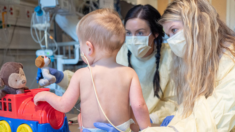 Two masked providers examine a toddler