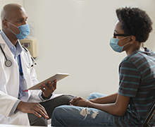 A male teen sitting facing a male provider who is holding a list of questions