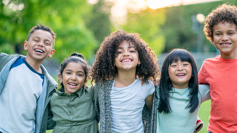 A group of kids with their arms wrapped behind each other smiling at the camera