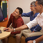 A boy and two adults look at a computer